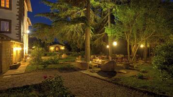 A well-lit outdoor area with a seating arrangement, surrounded by trees and a building with illuminated windows.