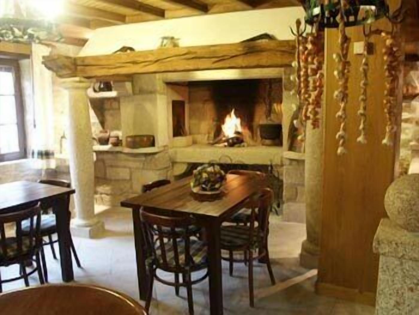 A rustic interior with a stone fireplace, wooden beams, and a dining area with a table and chairs.