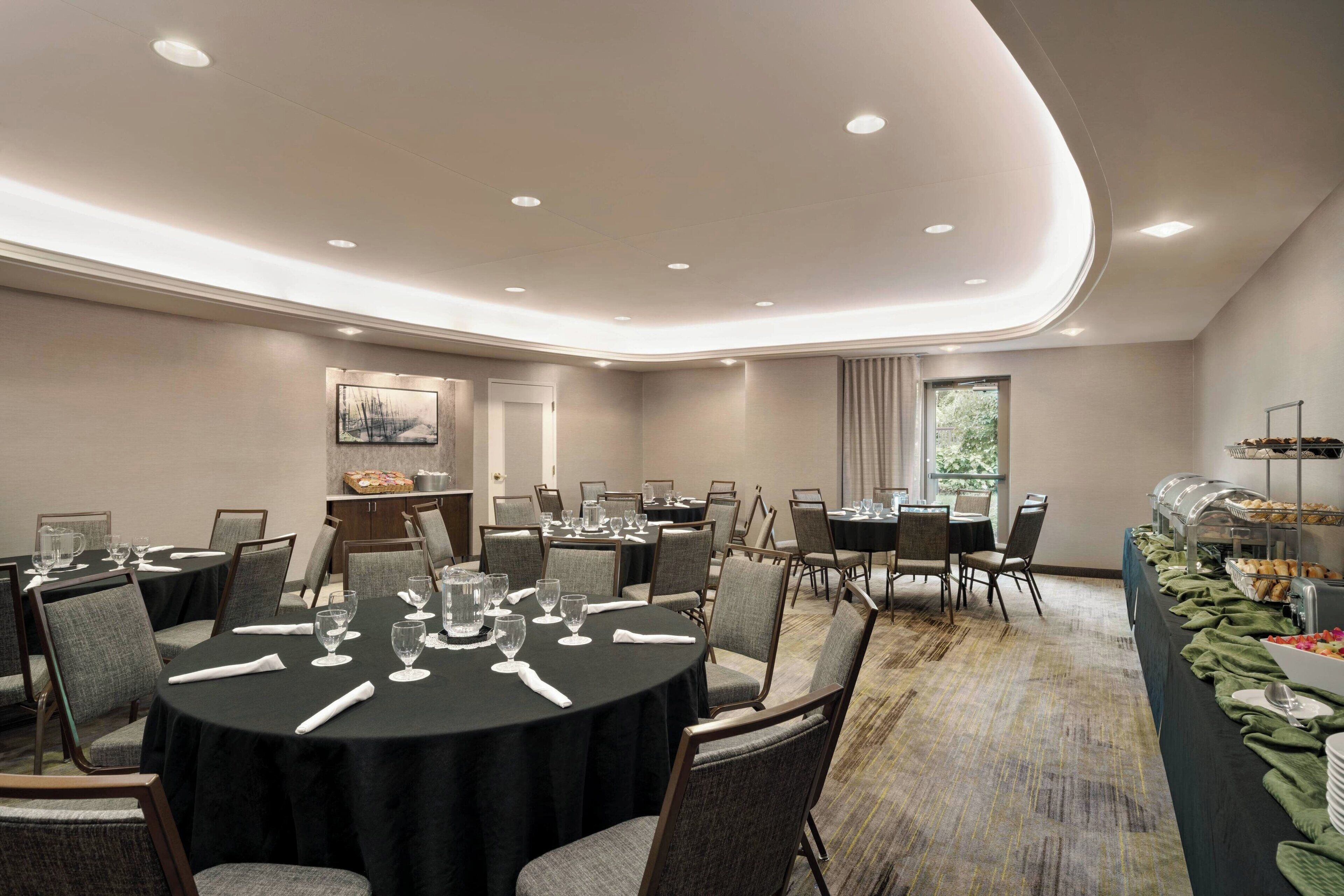 Una sala conferenze con tavoli rotondi, sedie e un'area buffet.