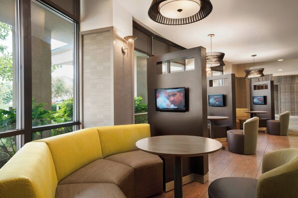 Un moderno vestíbulo de hotel con una zona de estar, ventanas amplias y una pantalla de televisión.