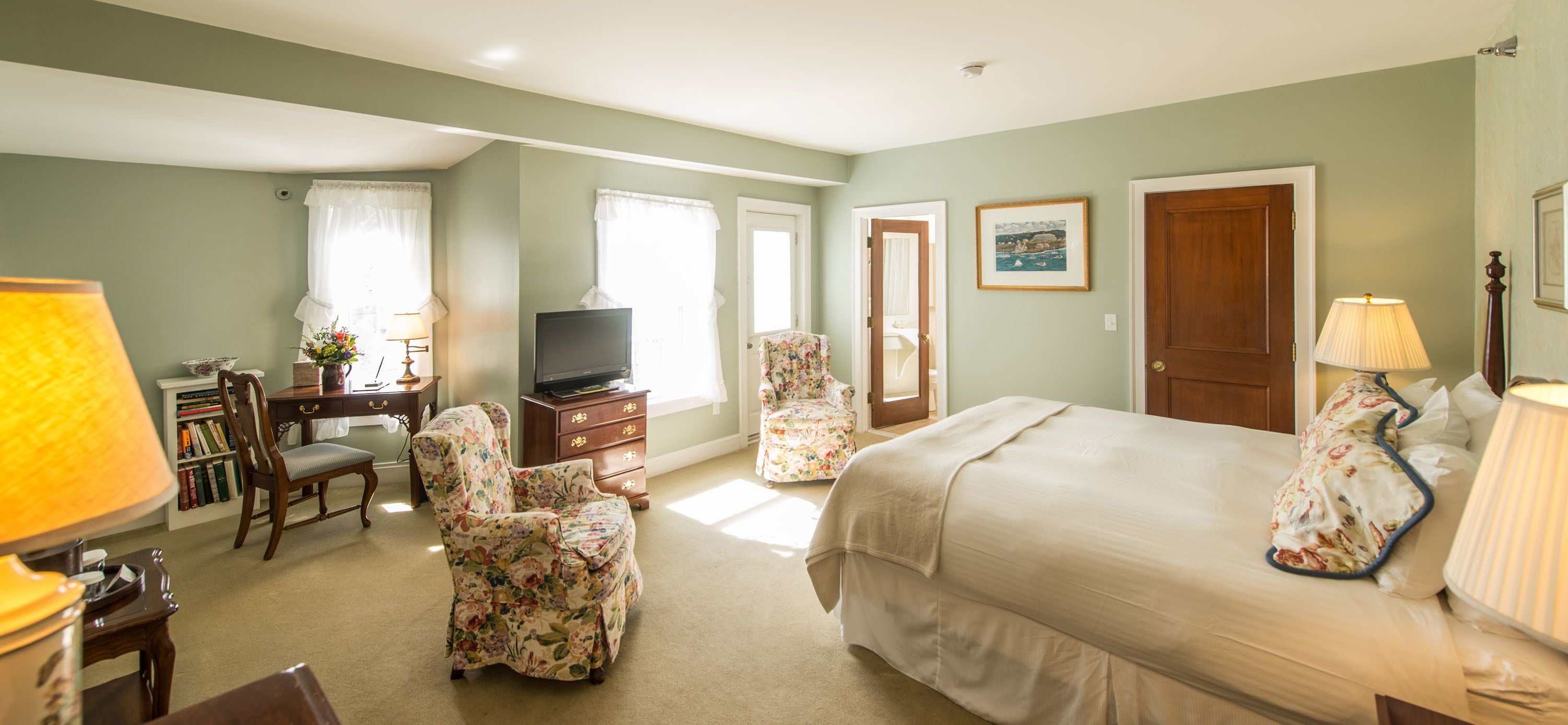 A bedroom with a large bed, a desk with a television, a chair, and a lamp.