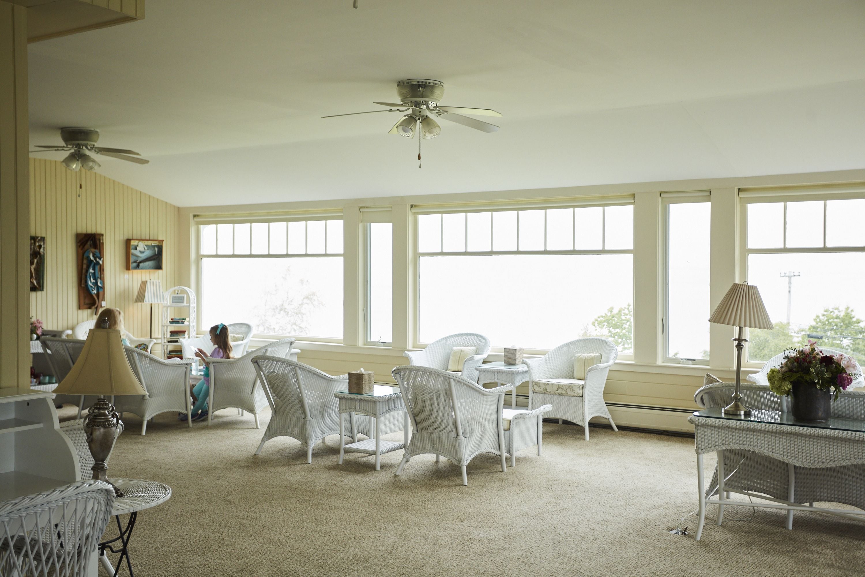 A spacious room with white wicker furniture, large windows, and ceiling fans.