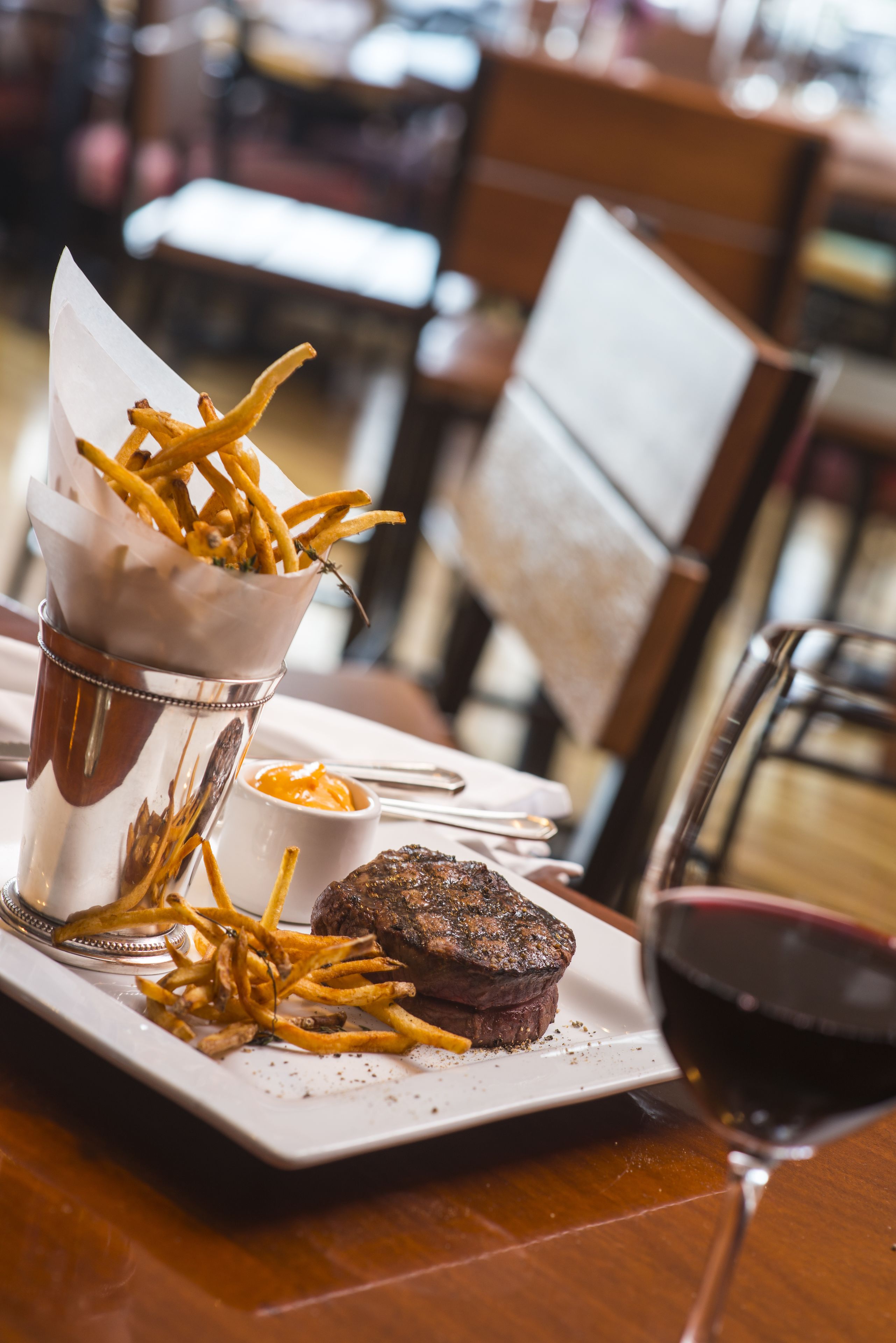 A plate with a steak, fries, and a glass of red wine on a wooden table.