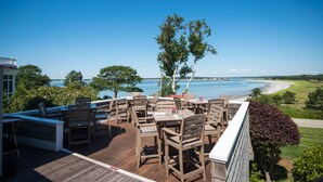 An outdoor deck with wooden furniture and a view of the beach and water. - Black Point Inn (Scarborough)