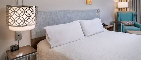 A hotel room with a large bed, a bedside table with a lamp, a chair, and a painting on the wall.