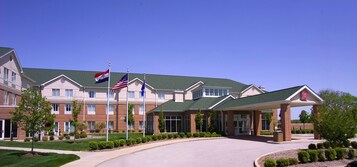 Un hotel de varios pisos con techo verde, entrada cubierta y banderas de Estados Unidos e India.