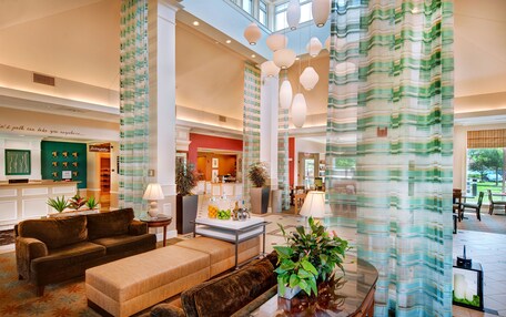 A spacious lobby with a high ceiling, a central seating area with sofas and a coffee table, and a large window providing natural light.