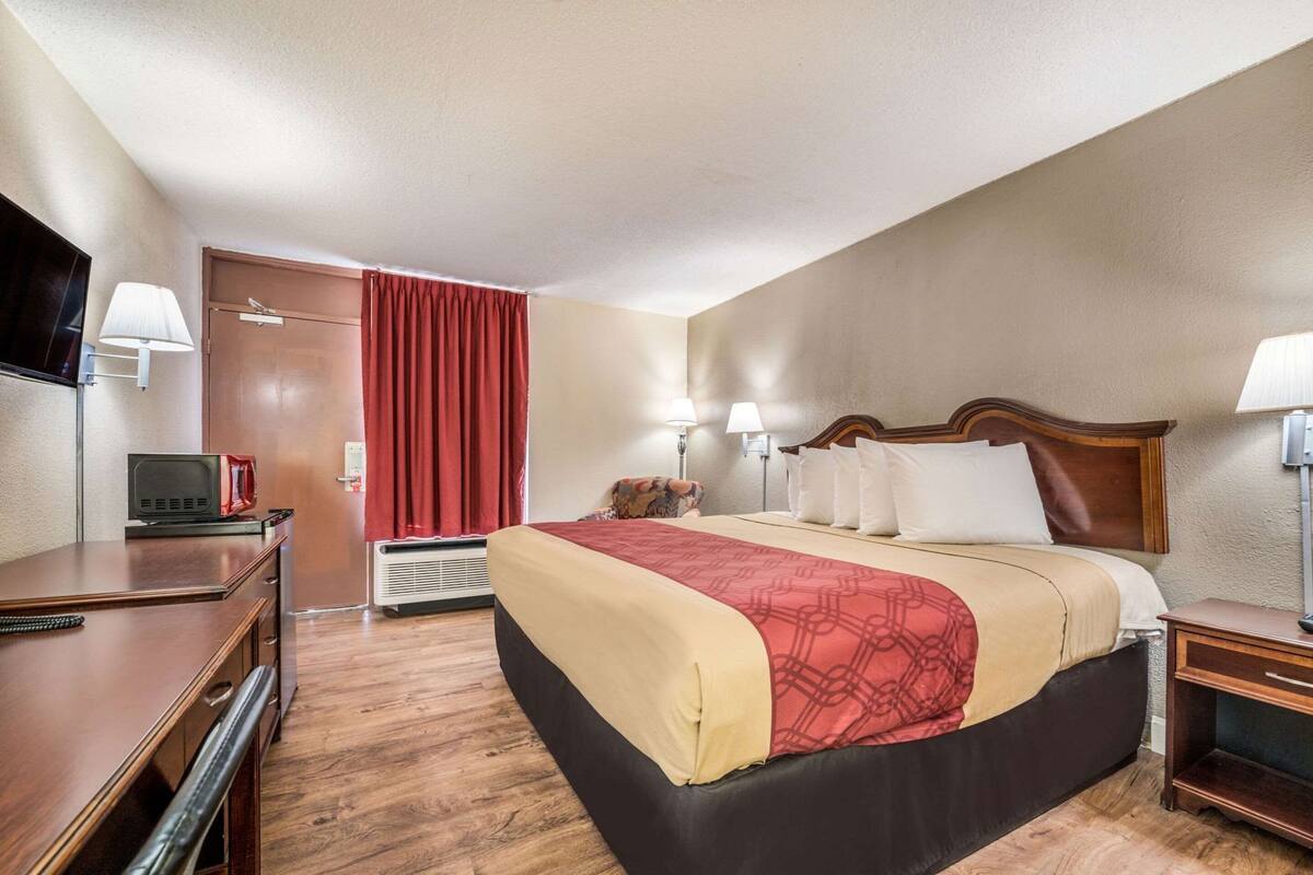 Une chambre d’hôtel avec un lit, des tables de chevet, un bureau, une télévision et un rideau rouge.