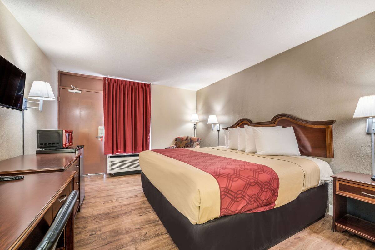 Une chambre d’hôtel avec un lit, des tables de chevet, un bureau, une télévision et un rideau rouge.