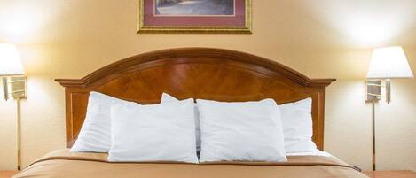A hotel room with a wooden headboard, two bedside lamps, a framed picture on the wall, and a red patterned bedspread.