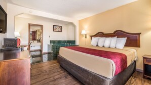 A hotel room with a large bed, wooden headboard, a desk with a lamp, a mirror, and a green-tiled wall. - Econo Lodge  Inn & Suites Macon West (Macon)