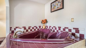 A bathroom with a large bathtub, a gold faucet, and a vase with flowers on the wall. - Econo Lodge  Inn & Suites Macon West (Macon)