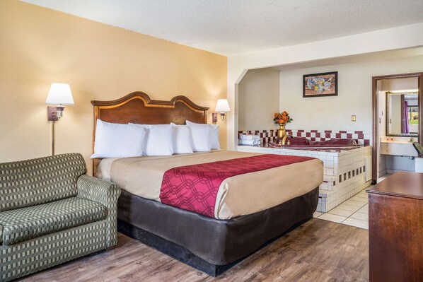 A hotel room with a bed, a sofa, a bathroom with a bathtub, and a small desk.