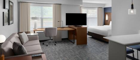Ein Hotelzimmer mit Bett, Schreibtisch mit Fernseher, einer Couch und einer kleinen Barzeile.