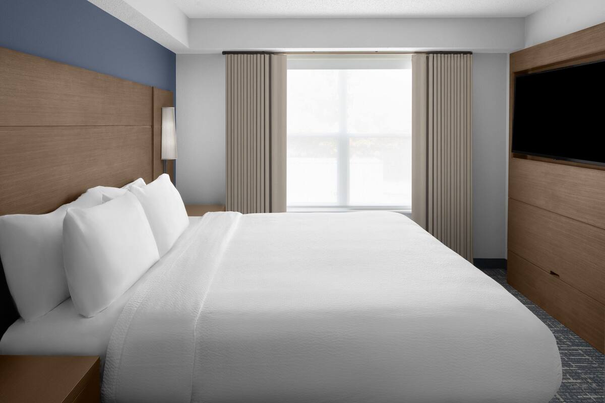 A hotel room with a large bed, a TV mounted on the wall, and a window with curtains.