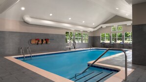 Een modern overdekt zwembad met helderblauw water, een betegeld zonnedek en een beschut gedeelte met zitplaatsen.