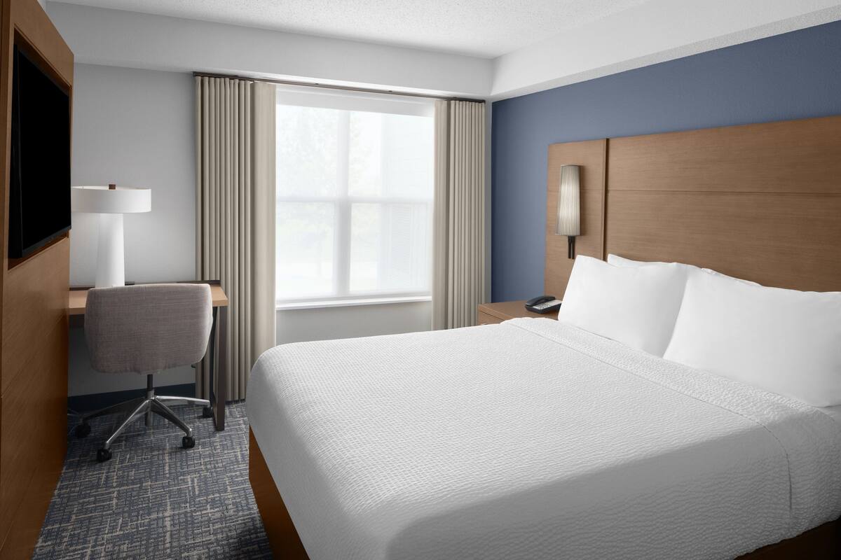 A hotel room with a large bed, a desk with a chair, a TV, and a window with curtains.