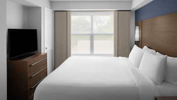 Une chambre d’hôtel avec un grand lit, un téléviseur posé sur une commode en bois et une fenêtre avec des rideaux.