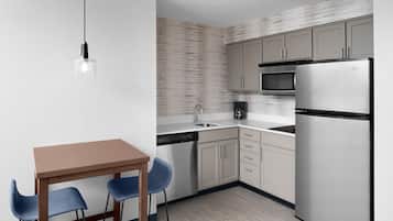 A modern kitchen with a wooden table, two blue chairs, a dishwasher, a refrigerator, and a microwave.