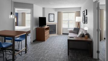 A hotel room with a bed, desk, chairs, a television, a fireplace, and a sofa.