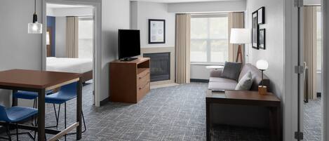 Una habitación de hotel con cama, escritorio, sillas, televisor, chimenea y sofá.