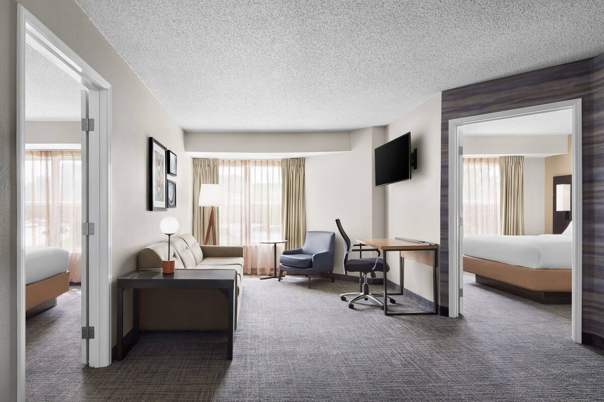 A hotel room with a bed, a desk, a chair, a TV, and a window with curtains.