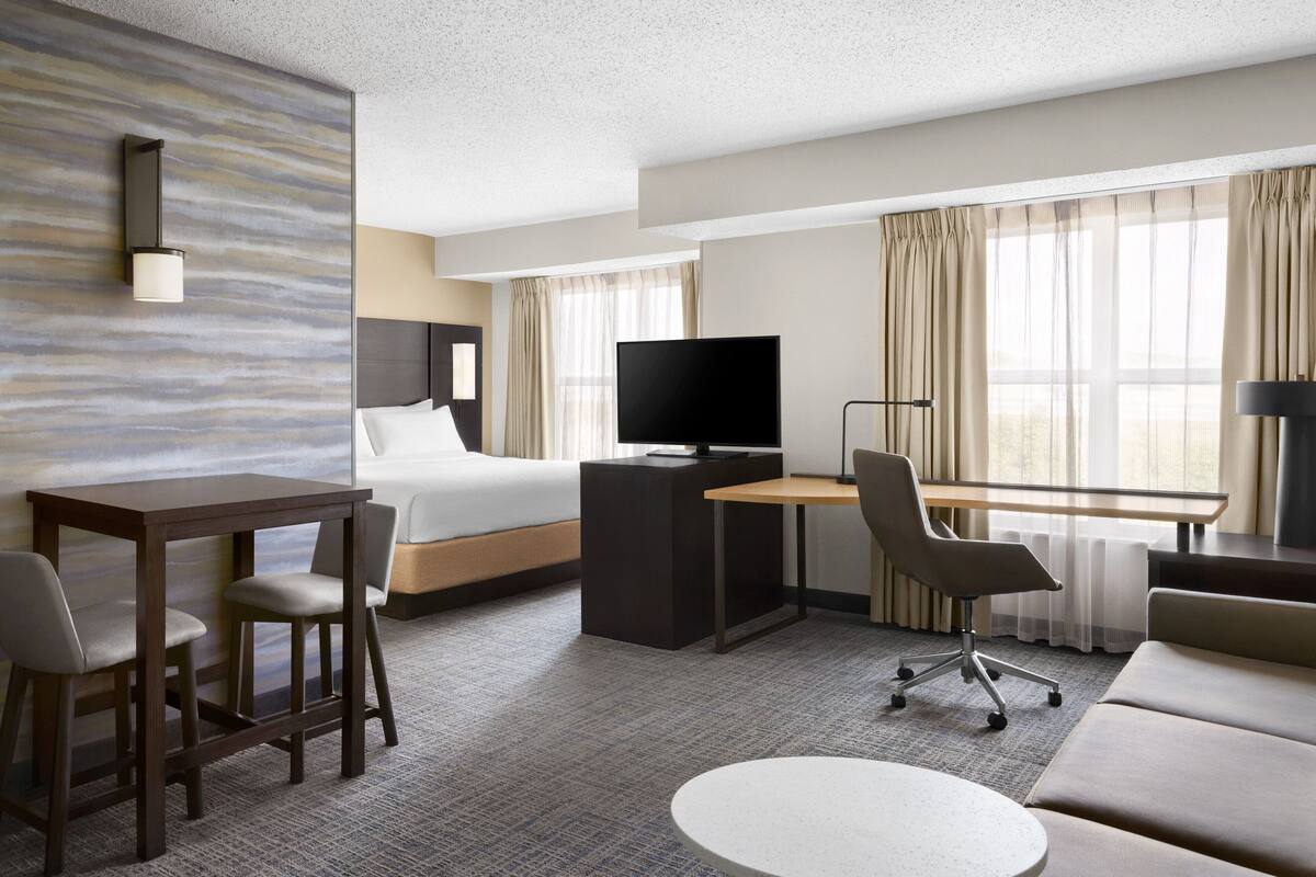 A hotel room with a bed, desk, TV, and seating area.