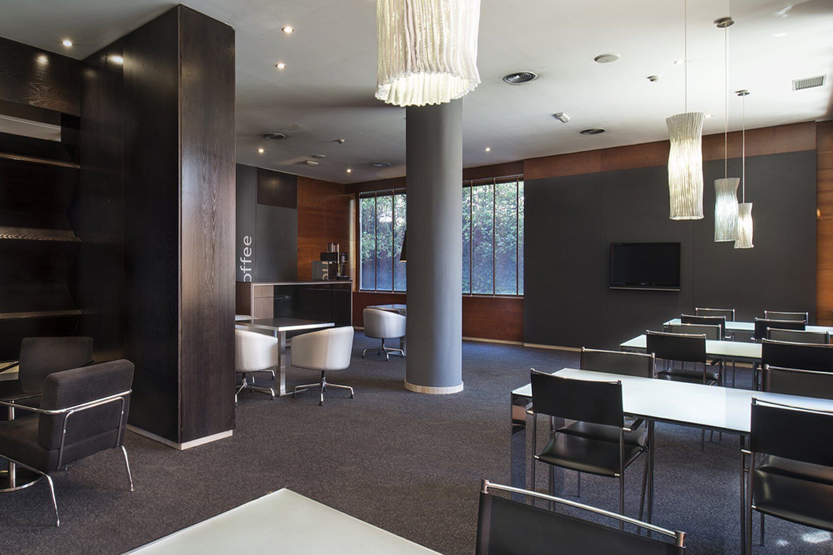 A modern conference room with a large table, several chairs, a coffee station, and a large window providing natural light.
