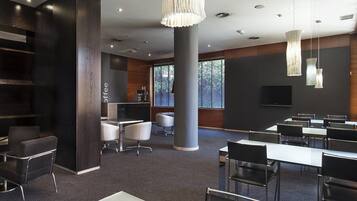 A modern conference room with a large table, several chairs, a coffee station, and a large window providing natural light.