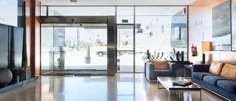 A modern lobby with a glass door entrance, a sofa, a coffee table, and a large abstract painting on the wall.