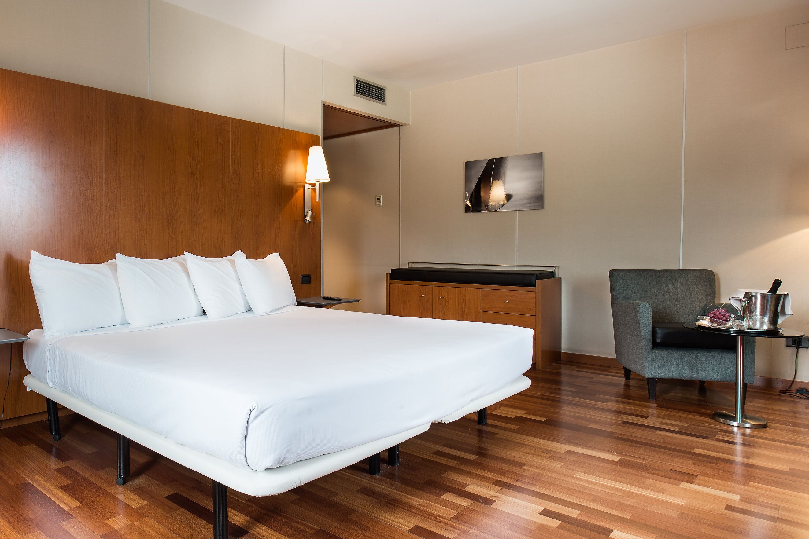 Une chambre d’hôtel avec un grand lit, une tête de lit en bois, un bureau avec une chaise et une lampe fixée au mur.
