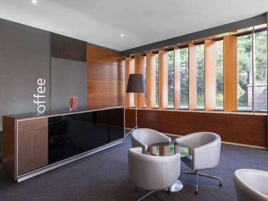 A modern office space with a large desk, two chairs, and a lamp.
