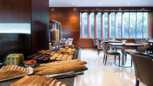 Un buffet de petit-déjeuner proposant une variété de viennoiseries et de pains, un coin café, ainsi qu’un espace détente avec des tables et des chaises.