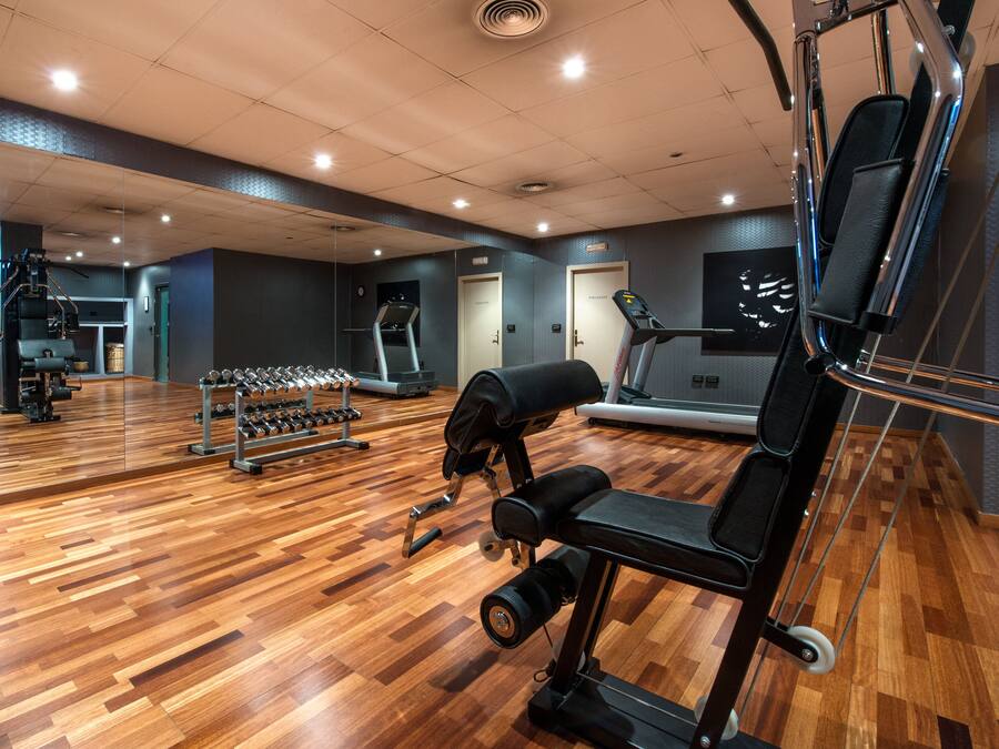 Un gimnasio con equipo de ejercicio, suelo de madera y paredes con espejos.