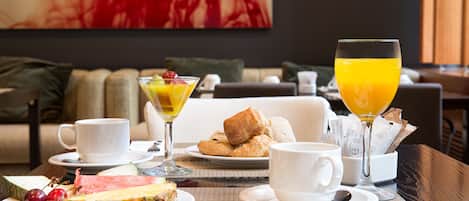 Una mesa de desayuno dispuesta para dos personas, con platos de comida, tazas y un vaso de zumo de naranja.