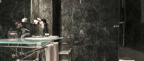 Un baño moderno con un lavabo de cristal, paredes de mármol, ducha y bañera.