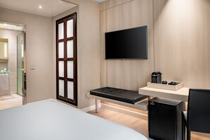 A modern hotel room with a bed, a desk with a chair, a flat-screen TV mounted on the wall, and a small coffee machine on a shelf. - AC Hotel Irla by Marriott (Barcelona)