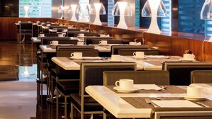 A modern restaurant with multiple tables and chairs, each set with a cup and saucer, and a long counter with a unique lamp design. - AC Hotel Irla by Marriott (Barcelona)