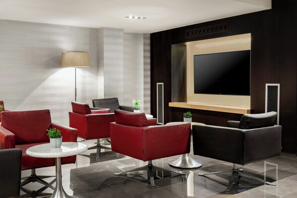 A modern lobby with red and black leather sofas, a marble table, a large flat-screen TV, and a floor lamp. - AC Hotel Irla by Marriott (Barcelona)
