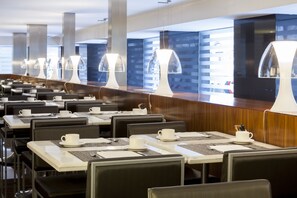 A modern dining area with multiple tables and chairs, equipped with white cups and saucers, and a long counter with a coffee machine. - AC Hotel Irla by Marriott (Barcelona)