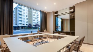A modern conference room with a large table, chairs, and large windows offering a view of a cityscape.