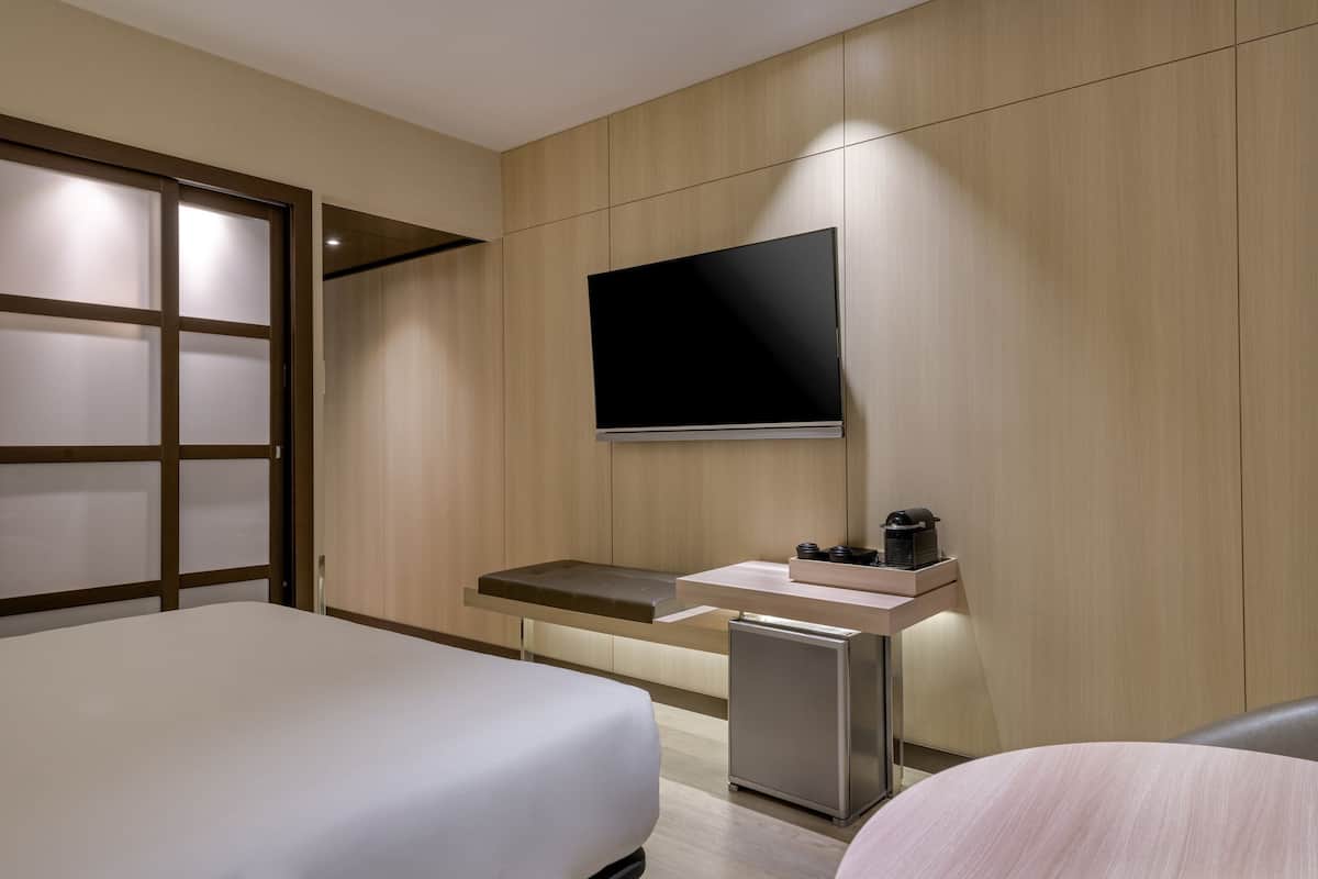 Een hotelkamer met een bed, een klein bureau met een koffiezetapparaat, een aan de muur bevestigde televisie en een schuifdeur.