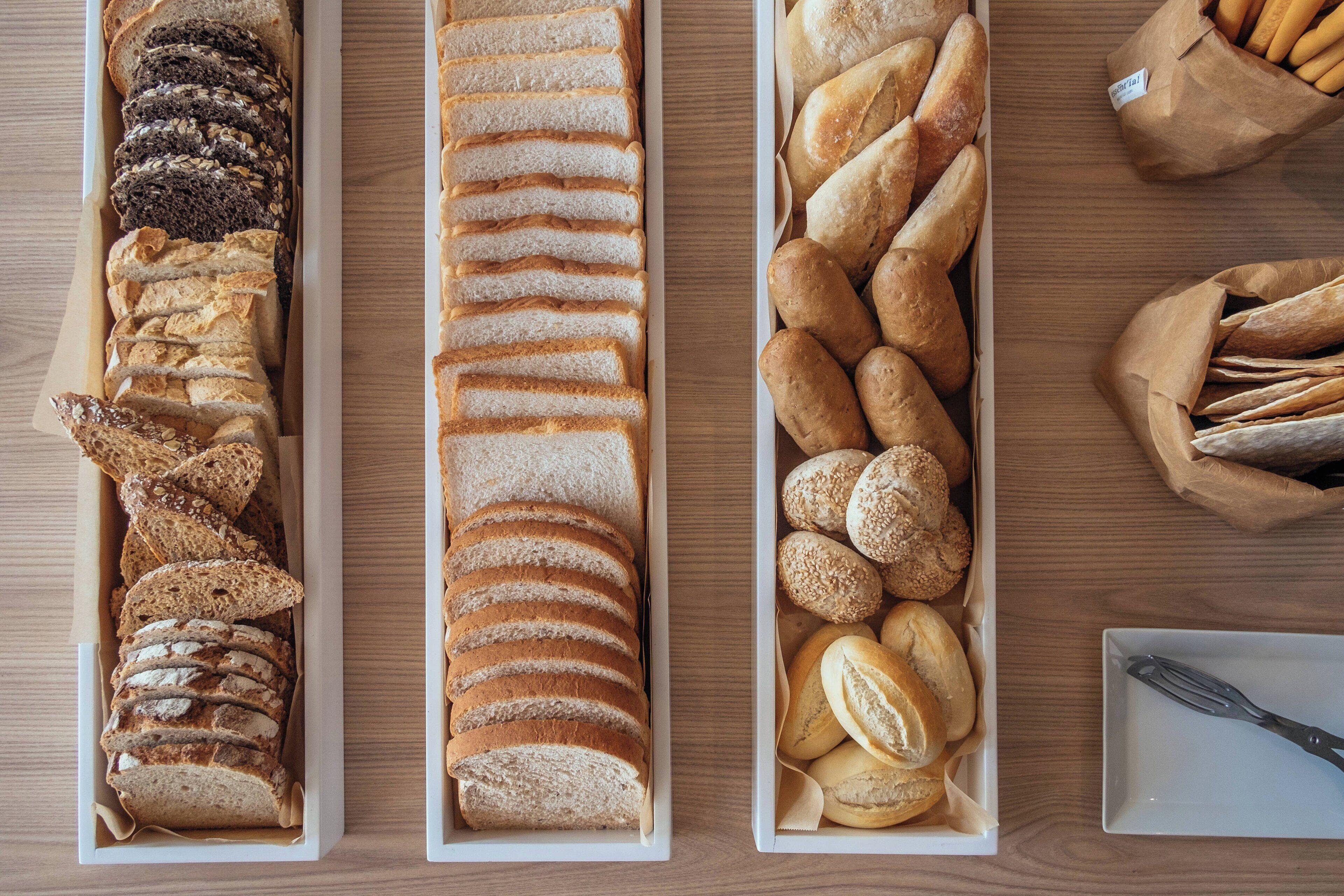Drei rechteckige Tabletts mit einer Auswahl an Brot auf einem Holztisch.