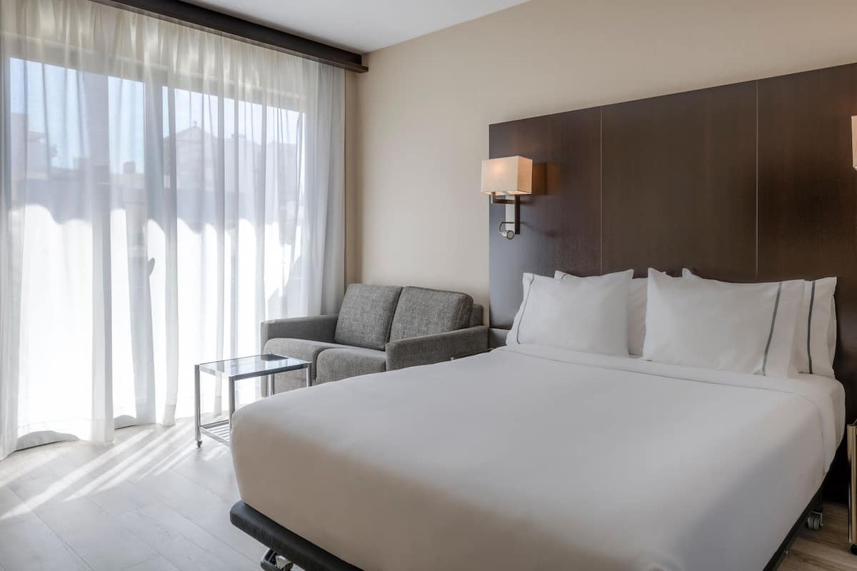 Een hotelkamer met een groot bed, een bank, een kleine tafel en een raam met dunne gordijnen.