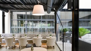 A modern indoor seating area with round tables and chairs, a large window with a view of greenery, and a hanging light fixture.