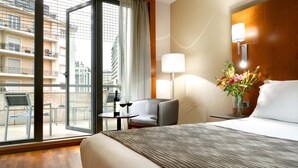 Una habitación de hotel con una cama, un escritorio con una silla, una lámpara y un florero con flores.
