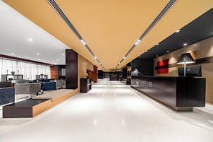 A modern hotel lobby with a reception desk, seating areas, and a long corridor.