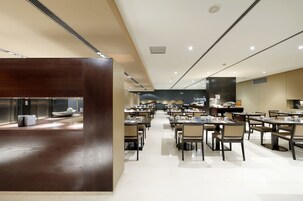 A spacious restaurant with multiple dining tables and chairs, a central counter, and a modern ceiling design.