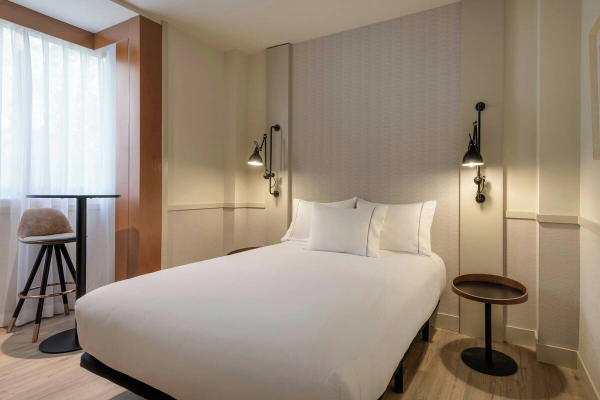 Una cama bien hecha con sábanas blancas en una habitación de hotel moderna.