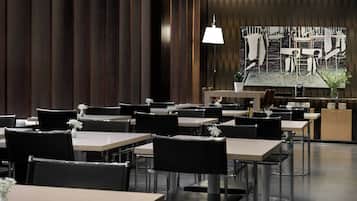 Ein modernes Restaurant mit mehreren Tischen und Stühlen, einem großen abstrakten Gemälde an der Wand und einer hängenden Leuchte.